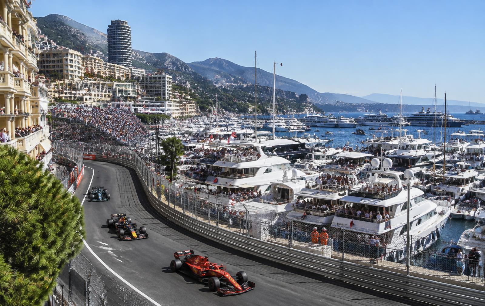 Formula 1 cars racing through the streets of Monte Carlo during the Monaco Grand Prix, with the harbor and yachts in the background