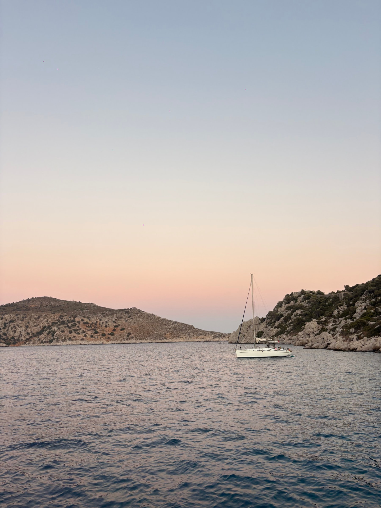 A sailboat anchored in a calm bay at sunset