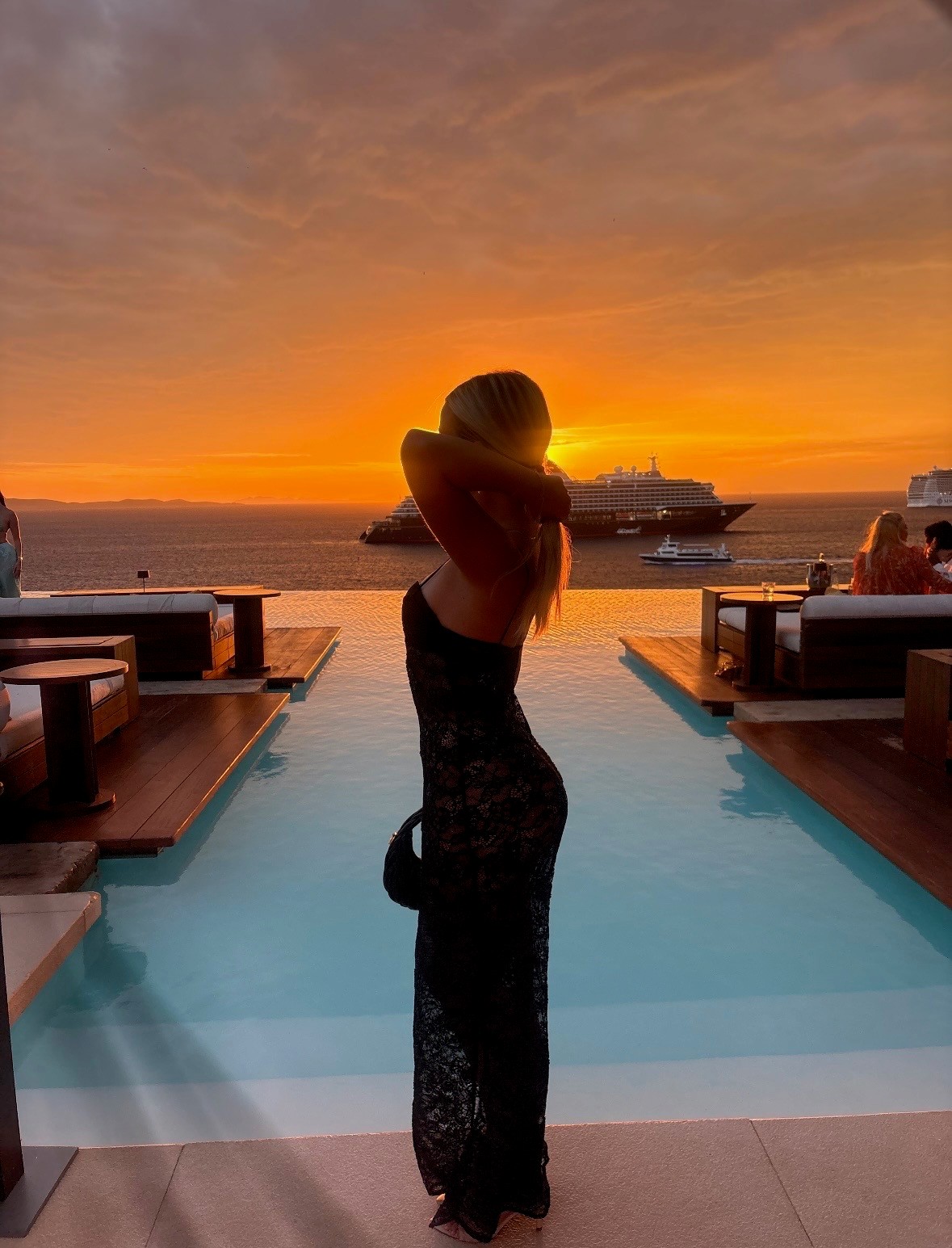 Teagan standing beside an infinity pool overlooking the sea at sunset